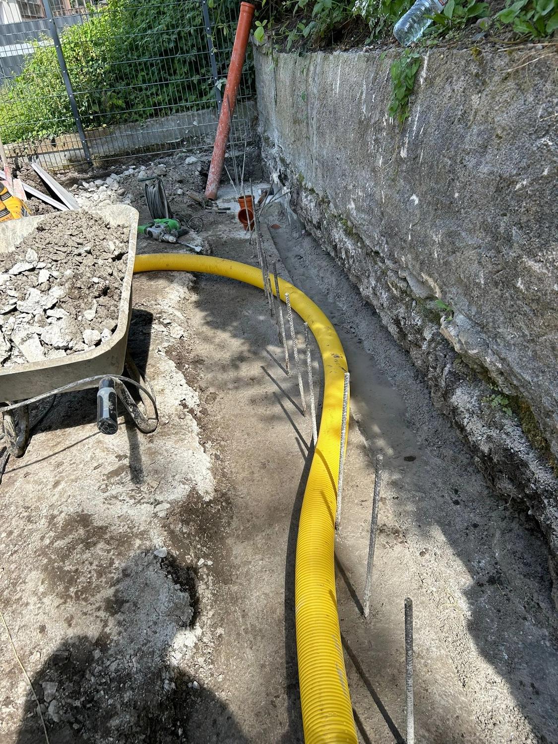 Offener Drainagegraben mit Bewehrung neben einer Steinmauer